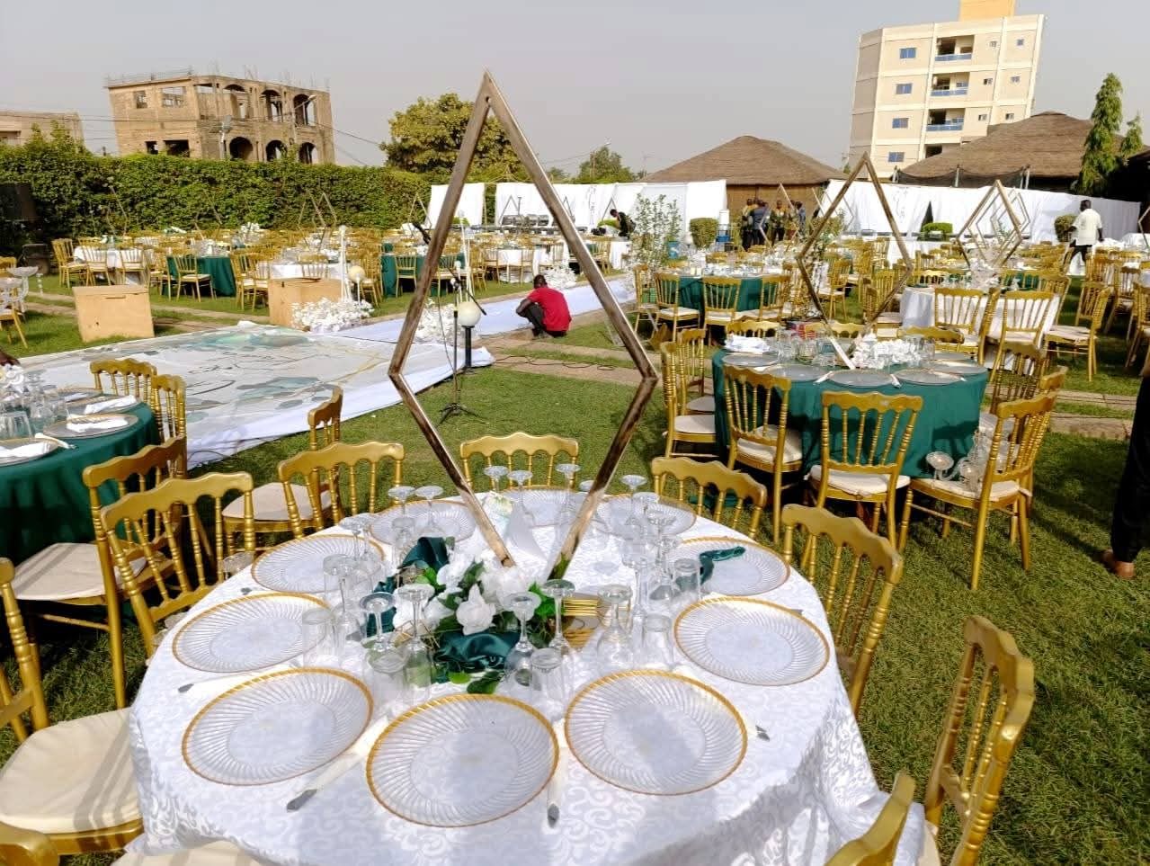Tables rondes dressées en blanc et or pour une réception de mariage dans le jardin